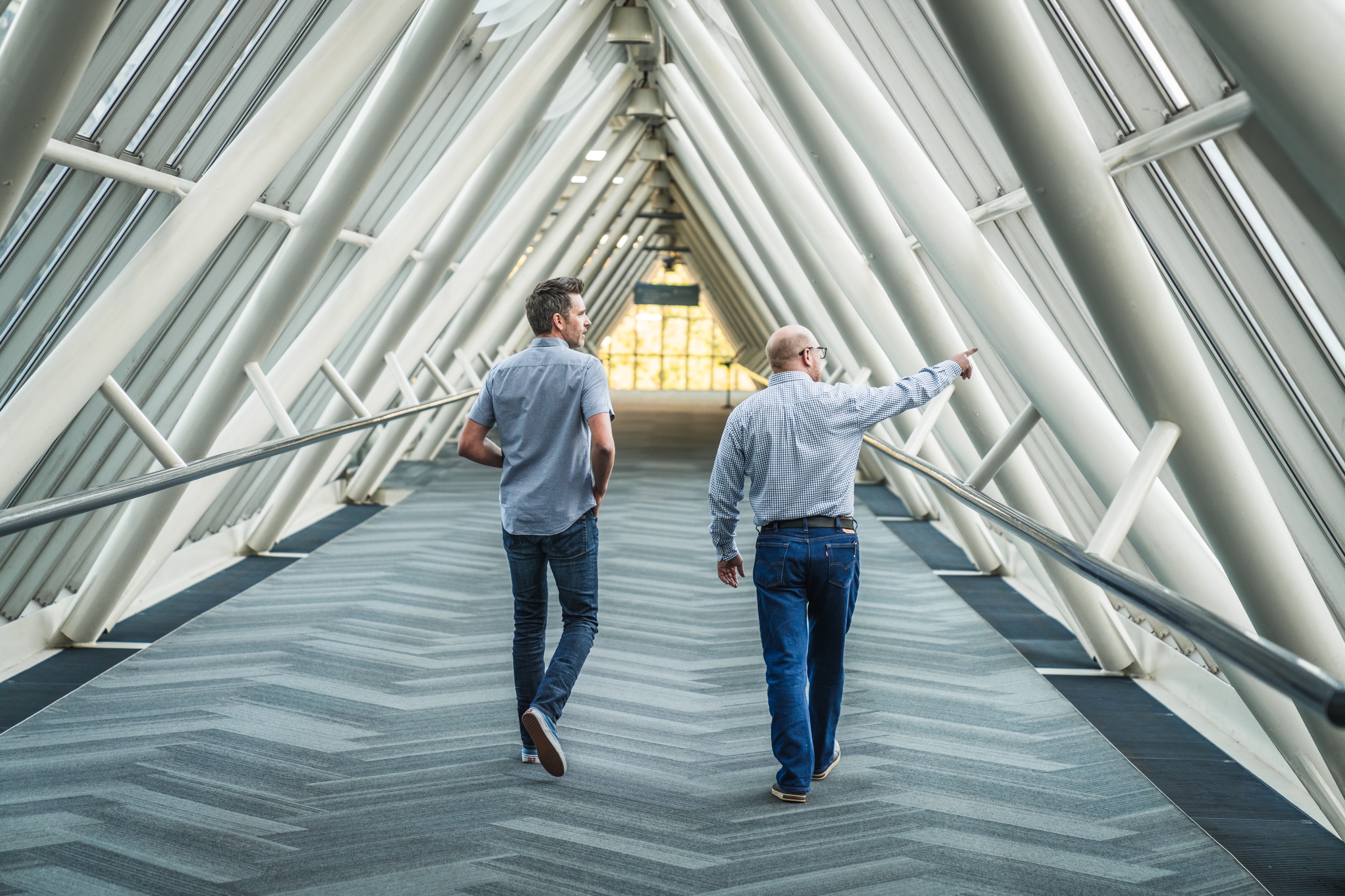 Two people walking through a bright building corridor